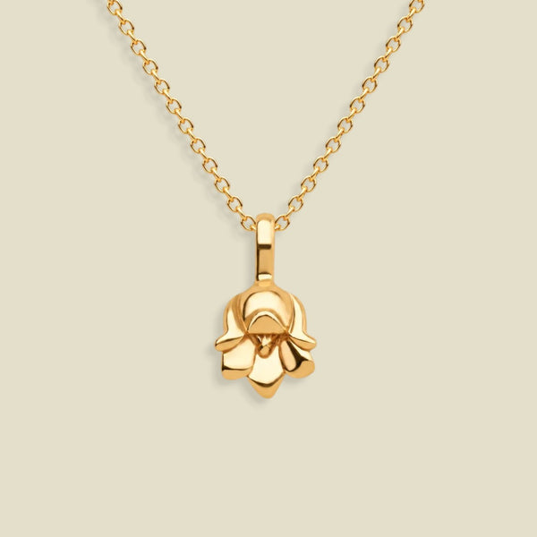 A polished yellow gold necklace with a small lily of the valley flower-shaped pendant, displayed against a solid light beige background.