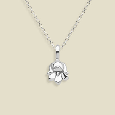 A polished silver necklace featuring a lily of the valley flower pendant, suspended from a delicate silver chain against a solid light beige background.