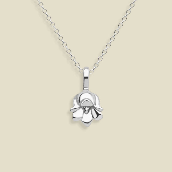 A polished silver necklace featuring a lily of the valley flower pendant, suspended from a delicate silver chain against a solid light beige background.