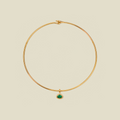 A delicate gold wire necklace with a small oval green gemstone pendant, displayed on a solid light beige background.