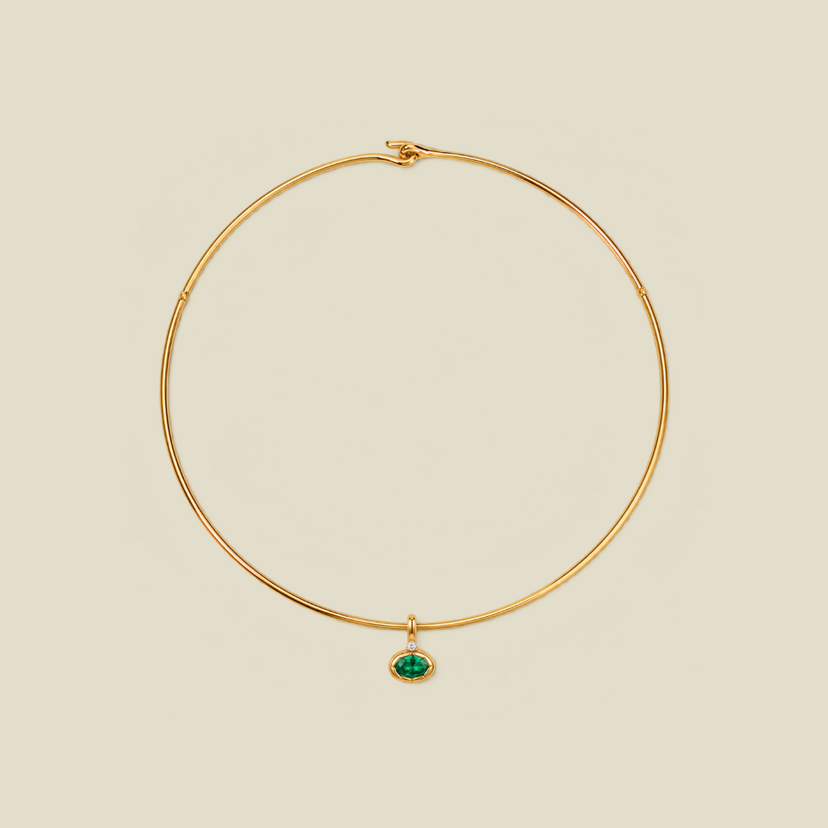 A delicate gold wire necklace with a small oval green gemstone pendant, displayed on a solid light beige background.