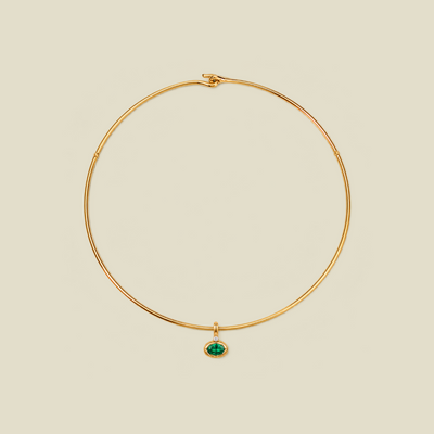 A delicate gold wire necklace with a small oval green gemstone pendant, displayed on a solid light beige background.