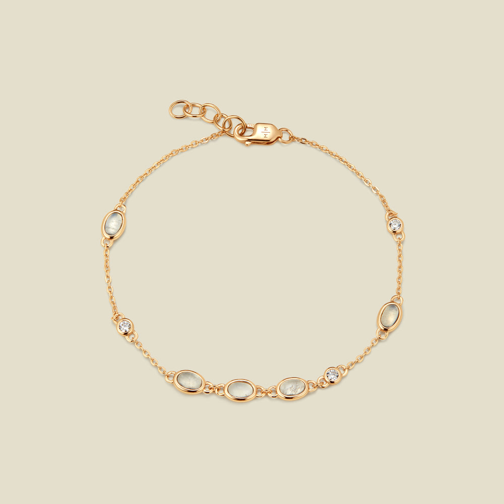 Gold bracelet with bezel-set white and clear stones against a neutral background.