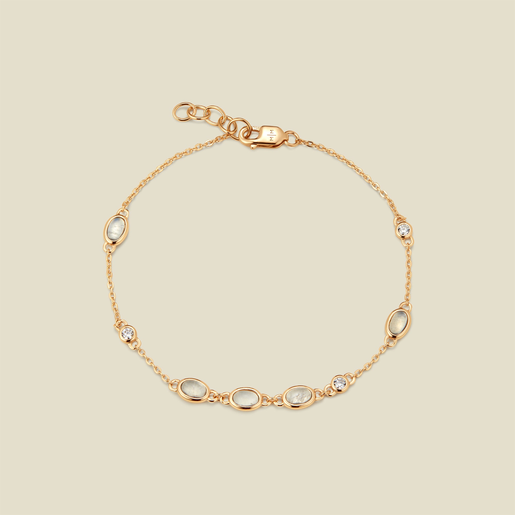 Gold bracelet with bezel-set white and clear stones against a neutral background.