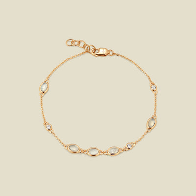 Gold bracelet with bezel-set white and clear stones against a neutral background.