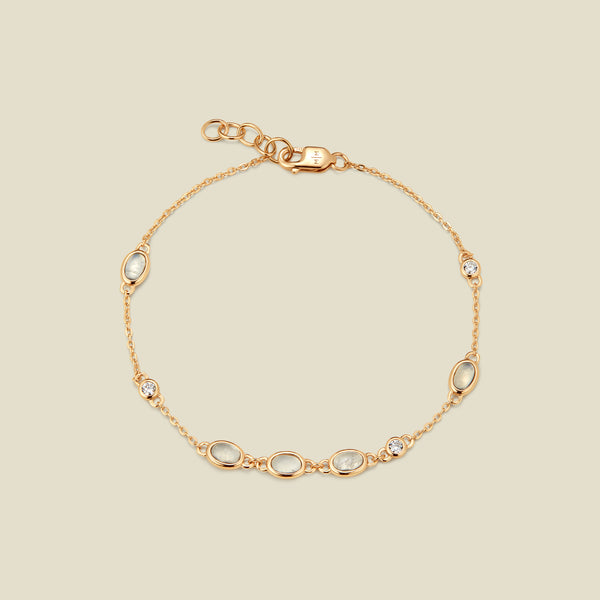 Gold bracelet with bezel-set white and clear stones against a neutral background.