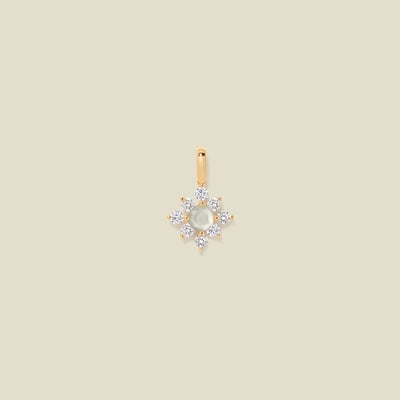 Gold charm with prong-set white and clear stones against a neutral background.