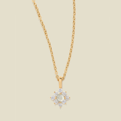 Gold chain with a white prong-set pendant against a neutral backdrop.