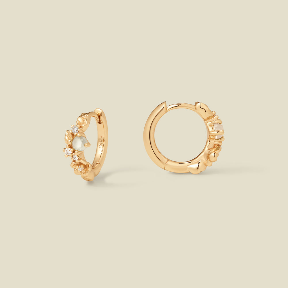 Gold hoop earrings with prong-set white and clear stones against a neutral background.
