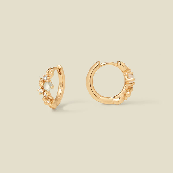 Gold hoop earrings with prong-set white and clear stones against a neutral background.