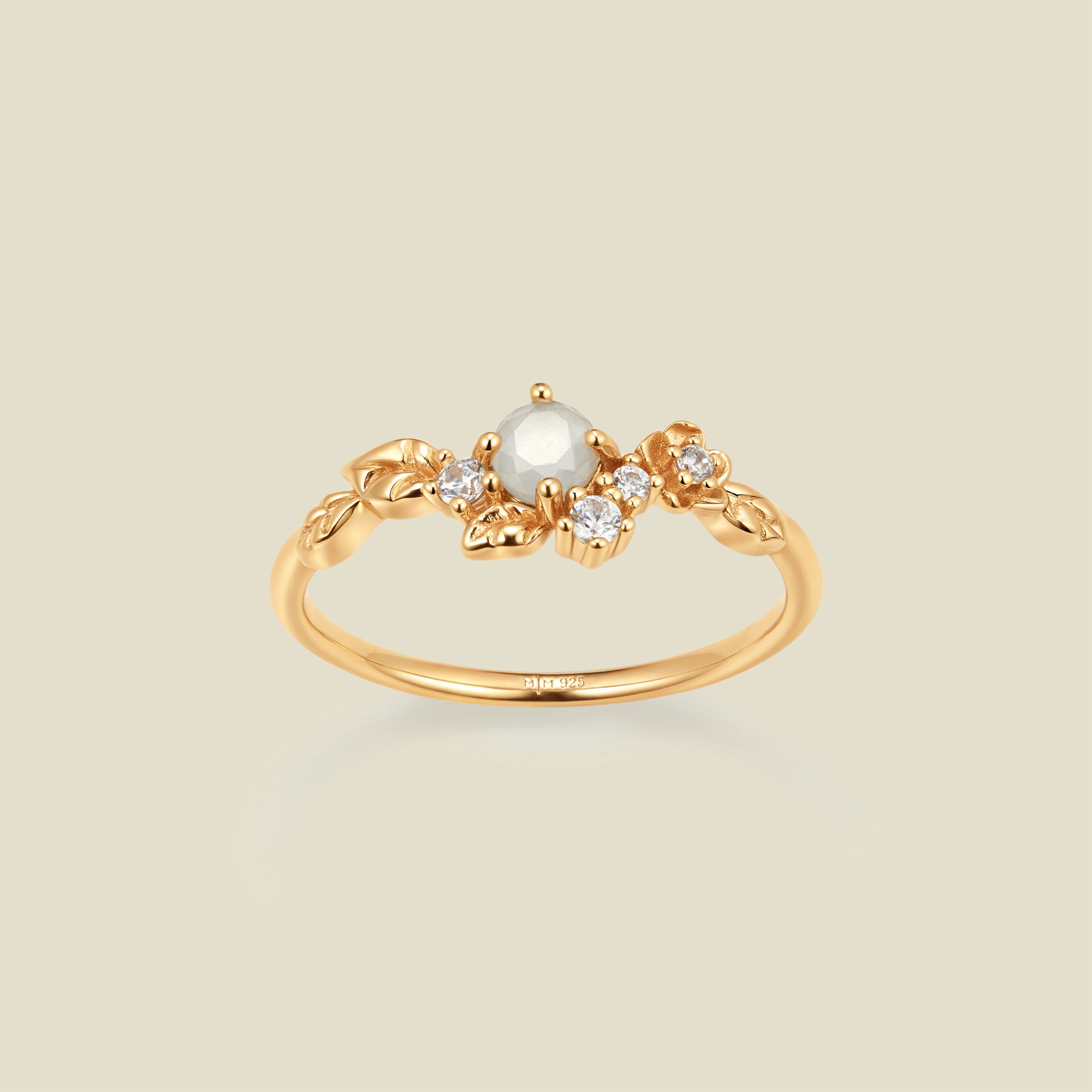 Gold ring with floral embellishments and white and clear prong-set stones against a neutral background.