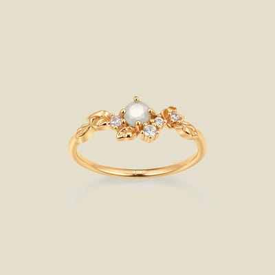 Gold ring with floral embellishments and white and clear prong-set stones against a neutral background.
