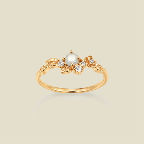 Gold ring with floral embellishments and white and clear prong-set stones against a neutral background.