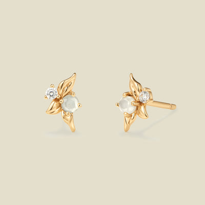 Gold stud earrings with prong set white and clear stones against a neutral backdrop.