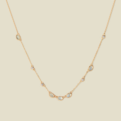Gold necklace with white and clear bezel-set stones against a neutral backdrop.