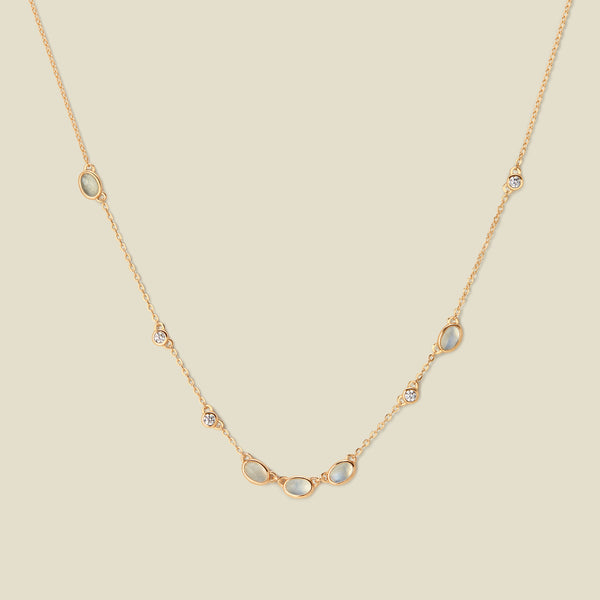 Gold necklace with white and clear bezel-set stones against a neutral backdrop.
