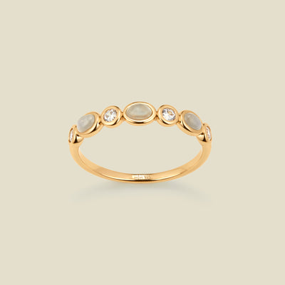 Gold ring with bezel-set white and clear stones against a neutral background.