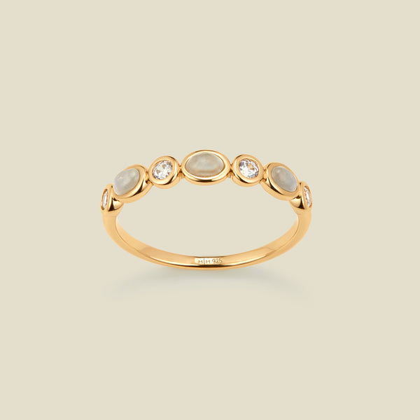 Gold ring with bezel-set white and clear stones against a neutral background.