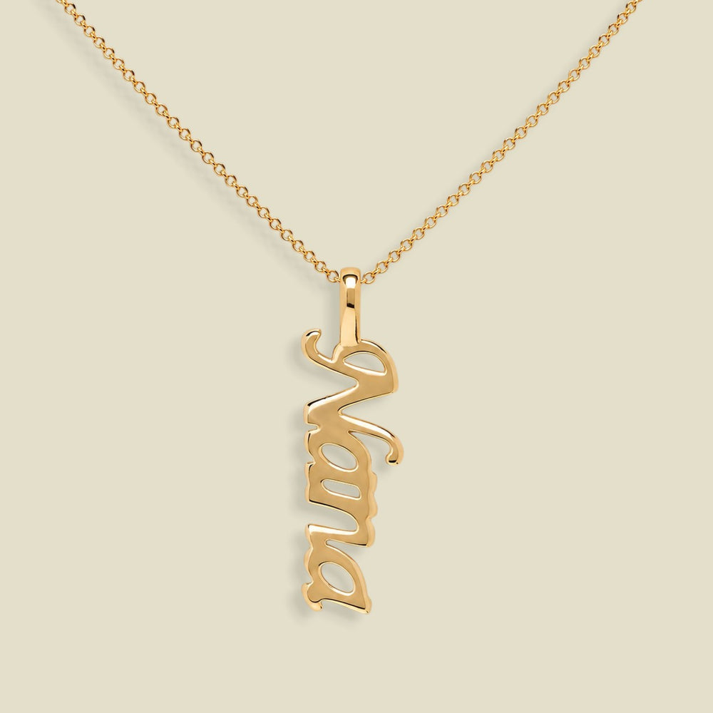 A gold nameplate necklace spelling 'Nana' in a cursive font, hanging vertically from a delicate gold chain against a solid beige background.