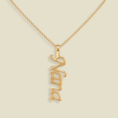 A gold nameplate necklace spelling 'Nana' in a cursive font, hanging vertically from a delicate gold chain against a solid beige background.