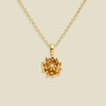 A gold chrysanthemum pendant necklace on a dainty gold chain, set on a soft beige background.