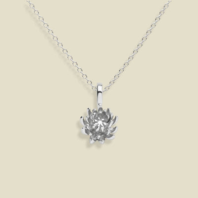 A silver chrysanthemum flower pendant necklace on a delicate silver chain, set against a solid light beige background.