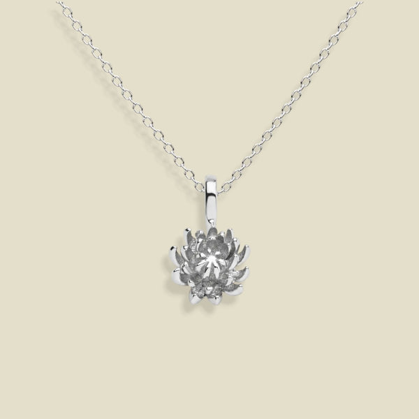 A silver chrysanthemum flower pendant necklace on a delicate silver chain, set against a solid light beige background.