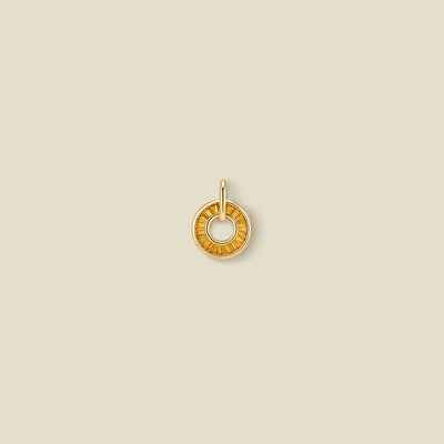 A gold circular pendant featuring golden yellow baguette-cut stones around a hollow center, displayed against a solid light beige background.