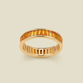 A gold eternity ring featuring a continuous channel setting of baguette-cut amber gemstones, shown on a solid light beige background.