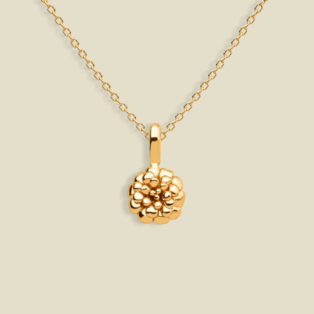 A gold necklace with a textured marigold flower pendant, displayed against a solid light beige background.