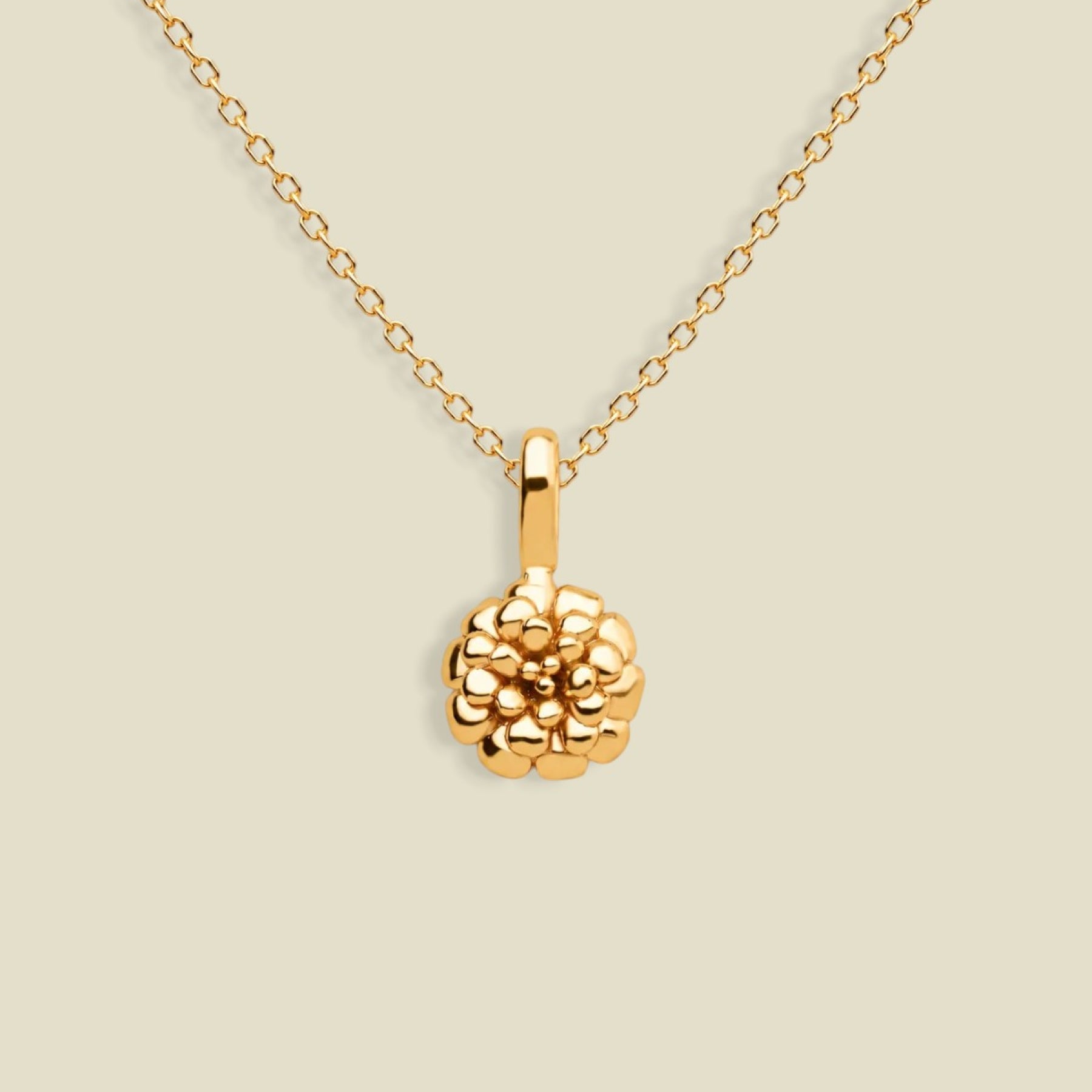 A gold necklace with a textured marigold flower pendant, displayed against a solid light beige background.