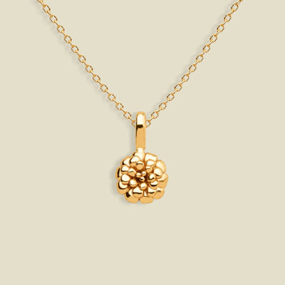 A gold necklace with a textured marigold flower pendant, displayed against a solid light beige background.
