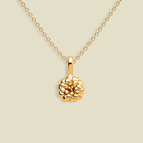 A gold necklace with a textured marigold flower pendant, displayed against a solid light beige background.