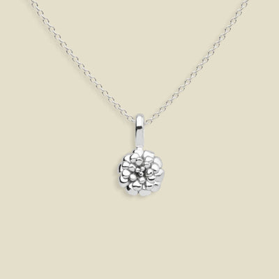 A silver marigold flower pendant necklace on a delicate silver chain, set against a solid light beige background.