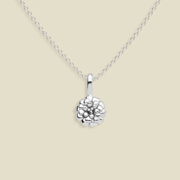 A silver marigold flower pendant necklace on a delicate silver chain, set against a solid light beige background.