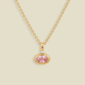 A delicate gold chain necklace with a small oval pendant featuring a pink gemstone and a tiny clear accent stone above it, set against a solid light beige background.