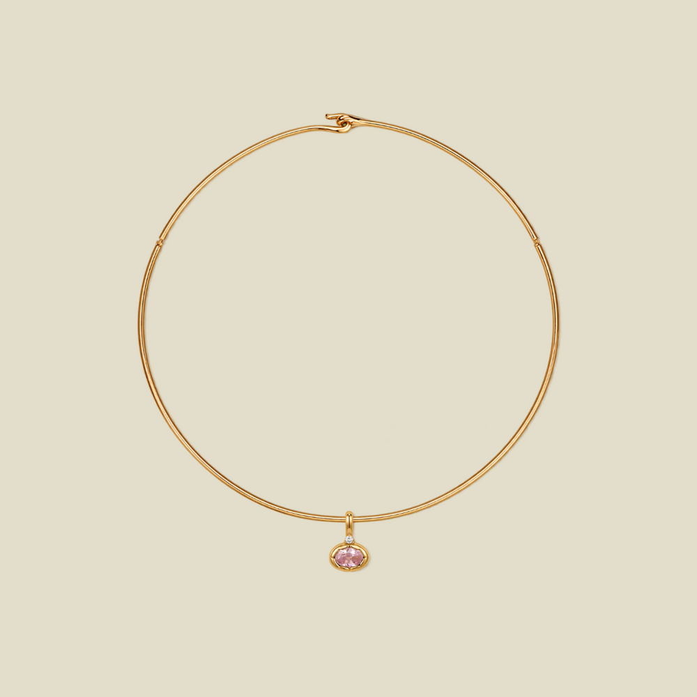 A delicate gold wire hoop necklace with a small oval-shaped pink gemstone pendant, displayed on a solid light beige background.
