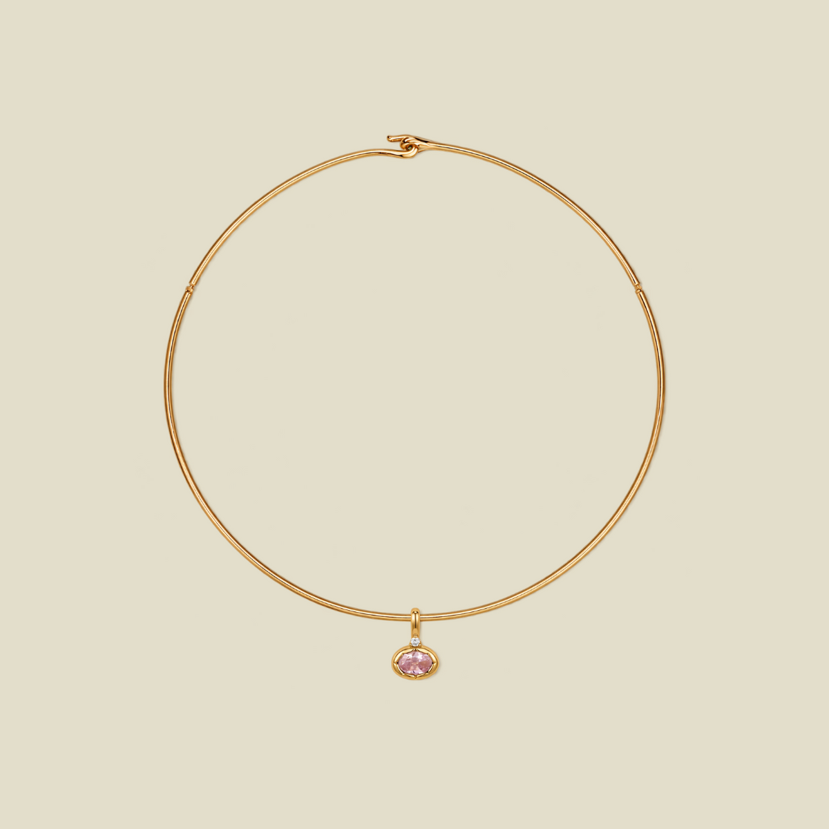 A delicate gold wire hoop necklace with a small oval-shaped pink gemstone pendant, displayed on a solid light beige background.