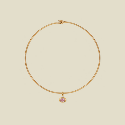 A delicate gold wire hoop necklace with a small oval-shaped pink gemstone pendant, displayed on a solid light beige background.