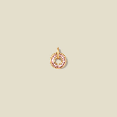 A circular gold pendant featuring pink baguette-cut stones around a hollow center, displayed against a solid light beige background.