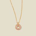 A gold chain necklace with a circular pendant featuring pink baguette-cut stones around a hollow center, displayed against a solid light beige background.