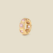 A small gold circular charm comprised of square, bezel-set pink gemstones side by side, set against a solid beige background.