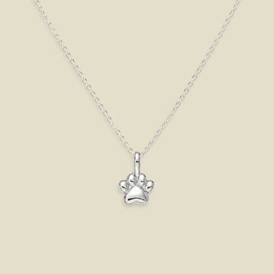 A silver paw print pendant necklace on a delicate silver chain, presented against a solid light beige background.