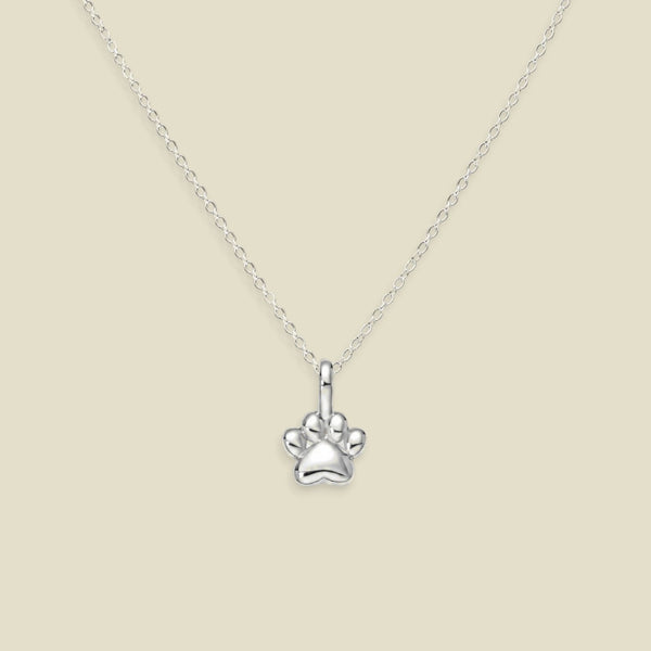 A silver paw print pendant necklace on a delicate silver chain, presented against a solid light beige background.
