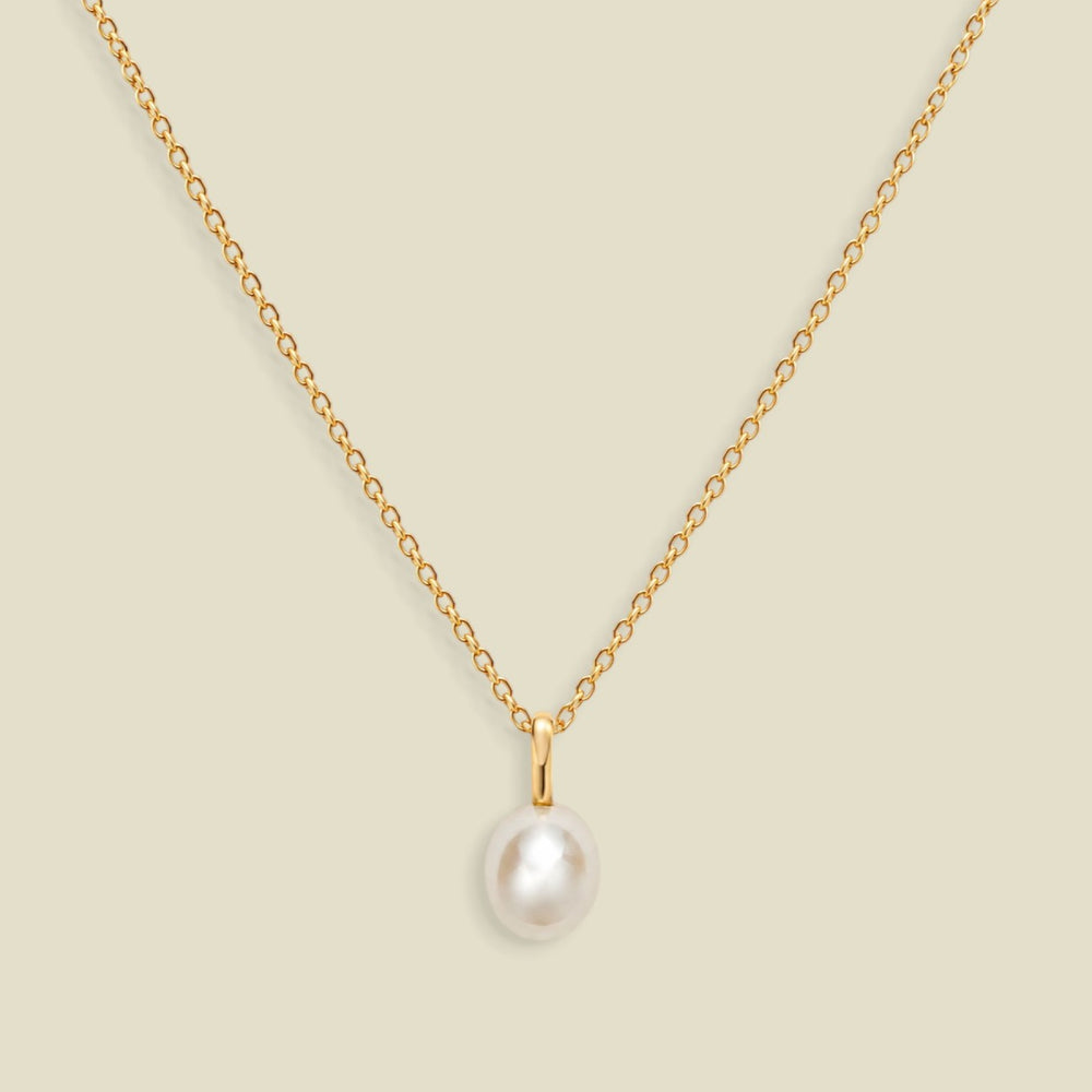 A gold dainty pendant necklace with a freshwater pearl charm, set on a solid soft beige background