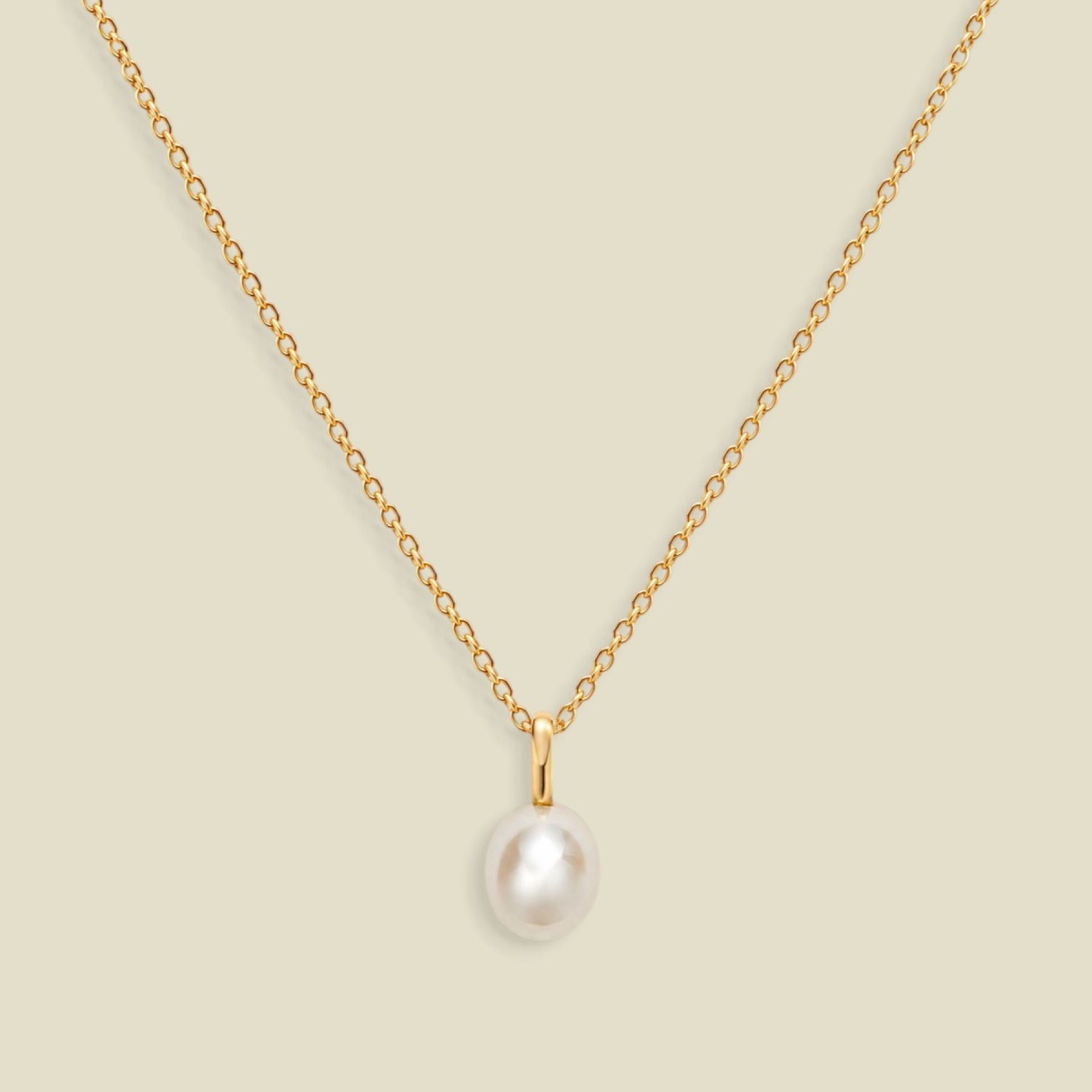 A gold dainty pendant necklace with a freshwater pearl charm, set on a solid soft beige background