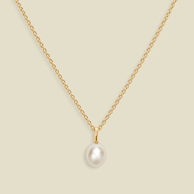 A gold dainty pendant necklace with a freshwater pearl charm, set on a solid soft beige background