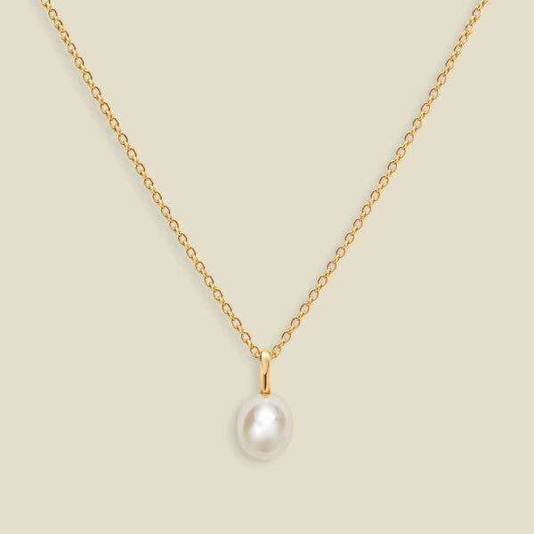 A gold dainty pendant necklace with a freshwater pearl charm, set on a solid soft beige background