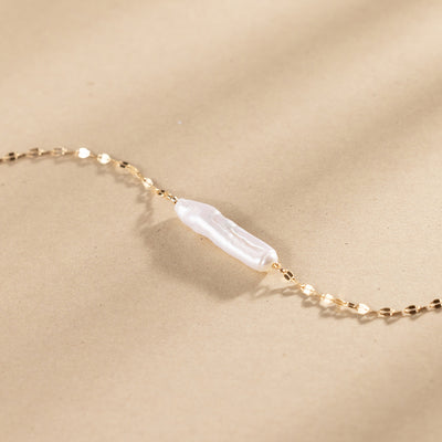 Gold necklace with a baroque pearl pendant against a plain beige background.