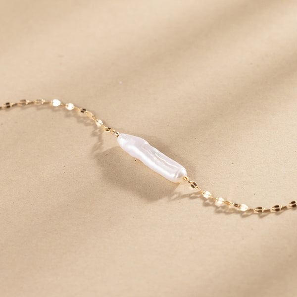 Gold necklace with a baroque pearl pendant against a plain beige background.
